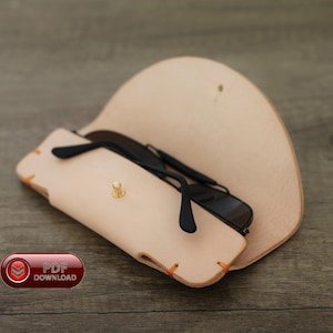 Puede incluir: Un estuche de cuero de color beige claro para gafas de sol con gafas de sol negras en su interior. El estuche está abierto, revelando las gafas. El estuche tiene costuras naranjas y un cierre dorado. La imagen también incluye un botón "PDF DOWNLOAD".