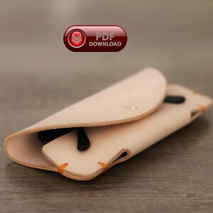 Puede incluir: Un estuche de gafas de cuero de color beige claro con gafas de sol negras en el interior. El estuche est&aacute; doblado y asegurado con un peque&ntilde;o bot&oacute;n de lat&oacute;n. Los bordes est&aacute;n cosidos con hilo naranja. El texto "PDF DOWNLOAD" es visible en la esquina superior izquierda.
