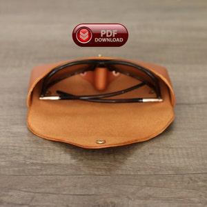 Puede incluir: Estuche de gafas de sol de cuero marr&oacute;n claro abierto, que revela un par de gafas de sol. El estuche es de color marr&oacute;n claro, con un cierre a presi&oacute;n dorado. Las gafas de sol tienen lentes oscuras y una montura negra. Tambi&eacute;n se ve un bot&oacute;n rojo con el texto "PDF DOWNLOAD".