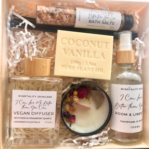 May include: A gift box filled with self-care items, including a coconut vanilla soap, a vegan diffuser, a candle with dried flowers, bath salts, and a room and linen spray. The products are all labelled with the phrase "I Can Love Me Better Than You Can".