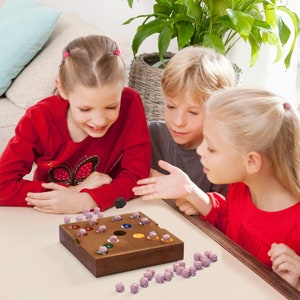 May include: Three children play a board game with colorful wooden pieces. The game board is made of wood and has a circular hole in the center. The children are sitting at a table and are focused on the game.
