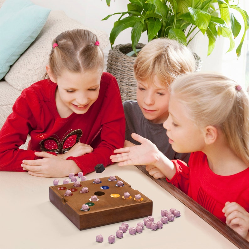 May include: Three children play a board game with colorful wooden pieces. The game board is made of wood and has a circular hole in the center. The children are sitting at a table and are focused on the game.