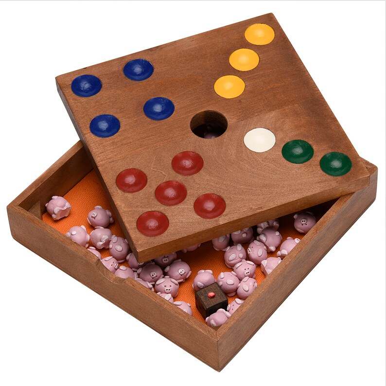May include: A wooden game board with a hole in the center and colored pegs in the corners. The board is open and the lid is off, revealing a compartment filled with small pink pig figurines.