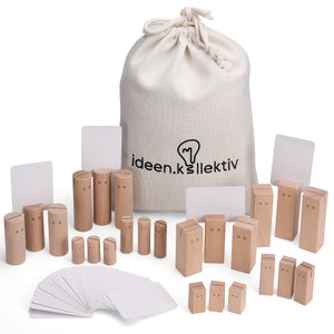Op de afbeelding: Een verzameling lichtgekleurde houten kaarthouders in diverse cilindrische en rechthoekige vormen, elk voorzien van een gleuf voor kaarten. Een beige canvas tas met trekkoord en de tekst ideen.kollektiv en een stapel blanco witte kaarten zijn inbegrepen.