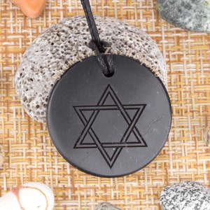 Puede incluir: Collar con colgante negro con una estrella de seis puntas tallada en la parte delantera. El colgante está hecho de piedra negra pulida y cuelga de un cordón negro.