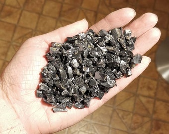 Könnte beinhalten: Eine Hand hält einen Haufen schwarzer Obsidian-Splitter. Die Splitter sind unregelmäßig geformt und haben eine glänzende, reflektierende Oberfläche.