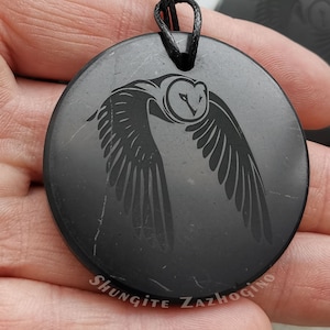 May include: Black shungite pendant with an engraved owl design. The pendant is round and has a black cord.