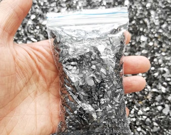 Könnte beinhalten: Ein durchsichtiger Plastikbeutel gefüllt mit kleinen, schwarzen, glänzenden, unregelmäßig geformten Glassplittern. Der Beutel wird in der Hand einer Person gehalten.