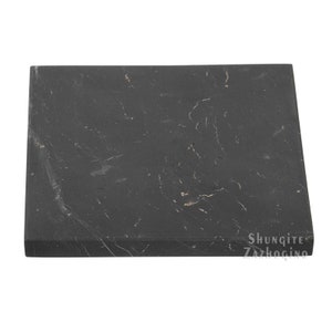 May include: A black square shungite slab with a smooth surface and a few white streaks. The slab is labelled "Shungite Zazhogino".