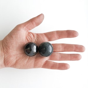 Peut inclure: Deux pierres lisses, rondes et polies. L'une est noire et l'autre est vert foncé. Les pierres reposent dans la paume d'une main.