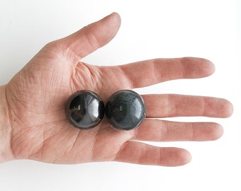 May include: Two smooth, round, polished stones. One is black and the other is dark green. The stones are resting in the palm of a hand.