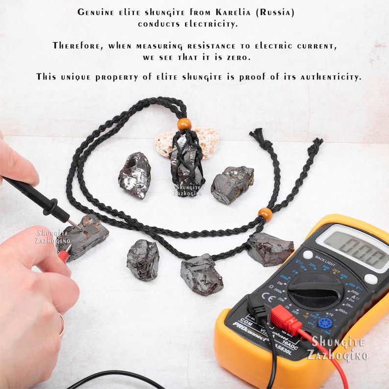 May include: A black braided cord necklace with a shungite pendant. The pendant is a rough, black stone with a silver sheen. The necklace is being tested with a multimeter to show that shungite conducts electricity. The multimeter reads 0.00. The text on the image reads "GENUINE Elite SHUNGITE FROM KARELIA (RUSSIA) CONDUCTS ELECTRICITY. THEREFORE, WHEN MEASURING RESISTANCE TO ELECTRIC CURRENT, WE SEE THAT IT IS ZERO. This UNIQUE PROPERTY of Elite Shungite is PROOF OF ITS AUTHENTICITY."