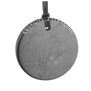 Puede incluir: Un colgante redondo de shungita negro con un cord&oacute;n negro. El colgante tiene las palabras "Shungite Zazhogono" inscritas alrededor del borde.