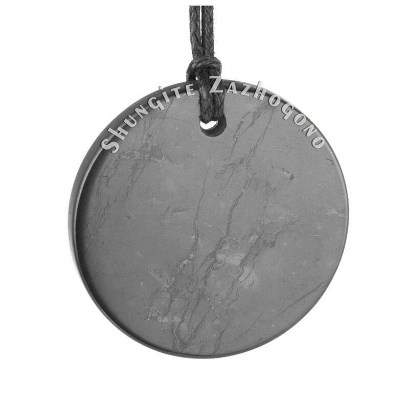 Puede incluir: Un colgante redondo de shungita negro con un cord&oacute;n negro. El colgante tiene las palabras "Shungite Zazhogono" inscritas alrededor del borde.