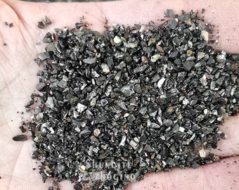 May include: A close-up of a handful of small, black, shiny, irregular-shaped pieces of crushed glass.