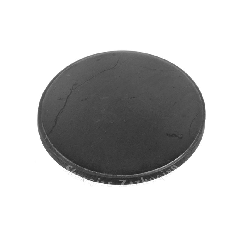 May include: A round, dark gray stone coaster with a slightly textured surface and a visible crack. The coaster has a thin, raised edge and the text "Shungite Zazhoking" is visible along the edge.