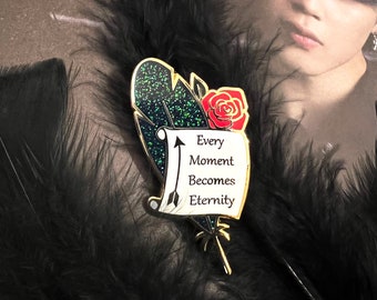 May include: A decorative pin featuring a feather design with a red rose and a scroll. The scroll reads "Every Moment Becomes Eternity" with an arrow. The feather has a dark blue and green glitter design.