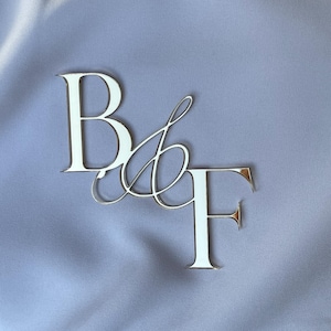 May include: Silver metal letters spelling "B & F" on a light blue fabric background.