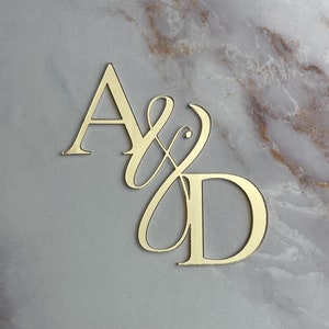 May include: Gold-coloured metal letters A and D with a stylised ampersand between them. The letters are on a marble background.