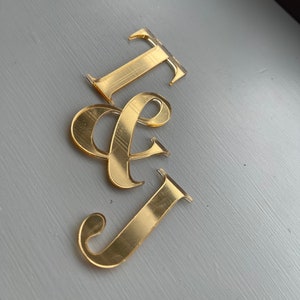 May include: Gold-coloured acrylic letters spelling "I & J" on a grey background.
