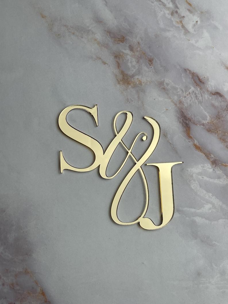 May include: Gold-colored metal initials "S & J" in a cursive script font. The initials are on a marble background.