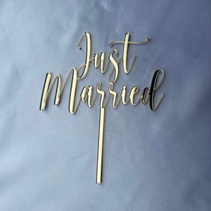 May include: Gold-coloured acrylic cake topper with the words "Just Married" in a cursive font.