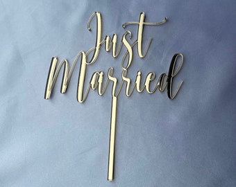 May include: Gold-colored acrylic cake topper with the words "Just Married" in a cursive font.