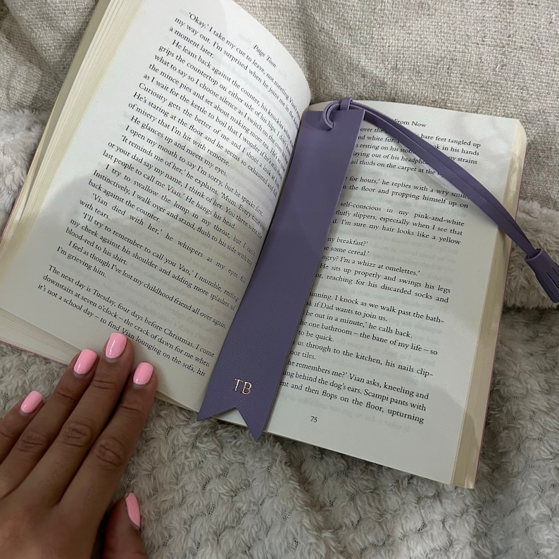 Purple Leather Bookmark with pointed arrow ends and detachable tassel with TB printed in rose gold, staged inside a book