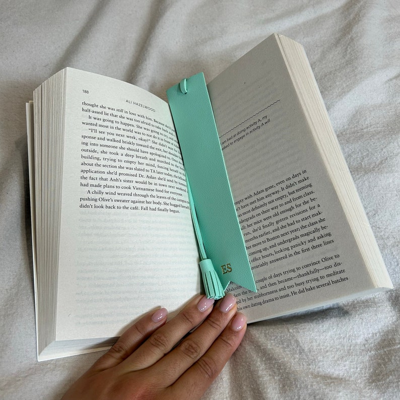 Turquoise Vegan Leather Bookmark with pointed arrow ends and detachable tassel with ES printed in gold, staged inside a book