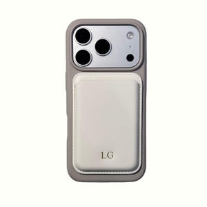 Könnte beinhalten: Eine graue Handyhülle mit einem weißen Kartenhalter. Das Gehäuse hat ein silbernes Kameramodul mit drei Objektiven und einem Blitz. Der Kartenhalter ist mit den Initialen "LG" geprägt.