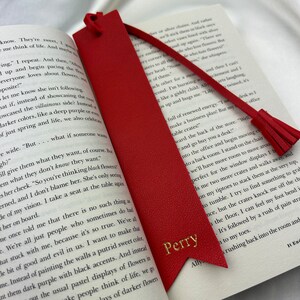 Red Vegan Leather Bookmark with pointed arrow ends and detachable tassel with Perry printed in gold, staged inside a book