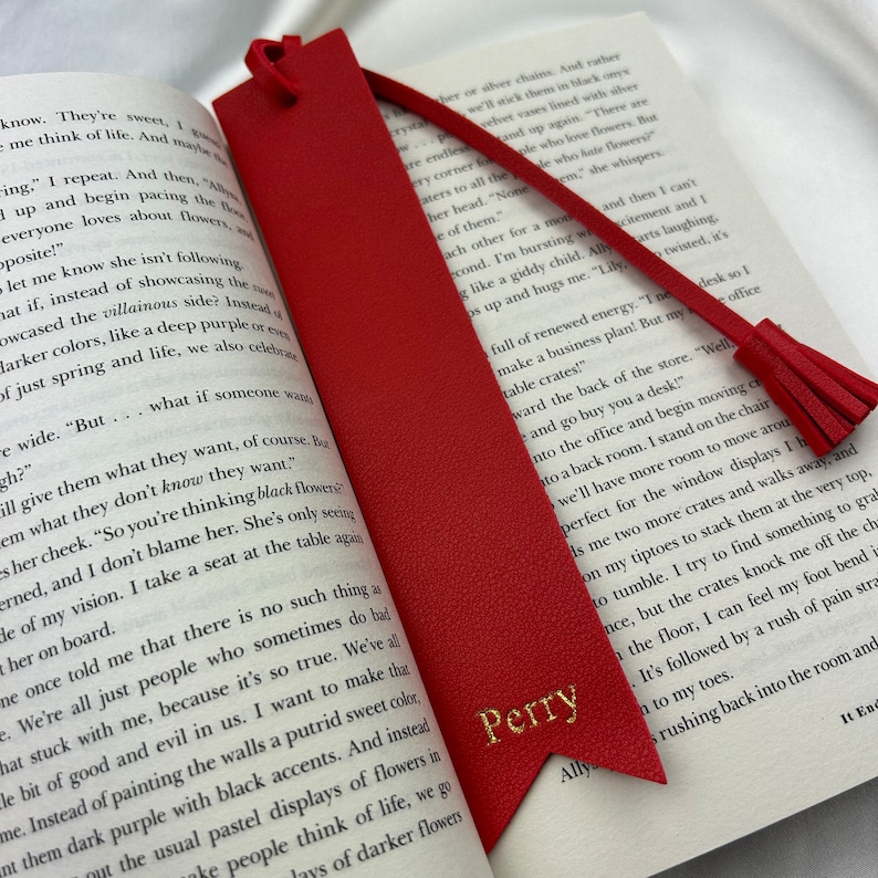 Red Vegan Leather Bookmark with pointed arrow ends and detachable tassel with Perry printed in gold, staged inside a book