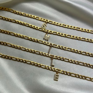May include: Five gold chain necklaces with letter charms. Each charm is encrusted with small clear rhinestones. The letters spell out the word "smile".