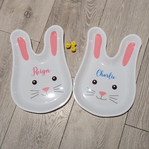 May include: Two white bunny-shaped plates with pink ears. The plate on the left says "Reign" and the plate on the right says "Charlie".