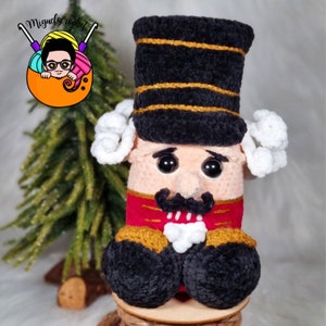 May include: A crocheted nutcracker doll with a black hat, red jacket, and white beard. The doll is sitting on a wooden base.
