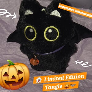 May include: A black plush creature with large yellow-rimmed eyes, pointed ears, and black wings. It wears a purple collar with a small orange pumpkin charm. Text on the image reads: Sopemates Collaboration, Limited Edition, Tangie.