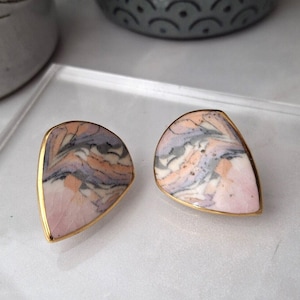 May include: A pair of teardrop-shaped earrings with a pink, white and grey marbled design. The earrings are set in gold.