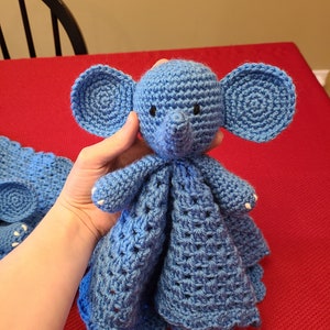May include: A blue crocheted elephant baby blanket with a soft, cuddly texture. The elephant has large ears and a small trunk.