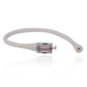 May include: A white rubber bracelet with a rectangular silver clasp featuring a pink and green gemstone surrounded by smaller diamonds and emeralds.