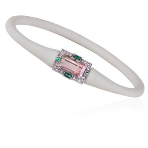 May include: A white silicone bracelet featuring a pink and green gemstone set in a silver frame. The gemstone is surrounded by smaller diamonds.