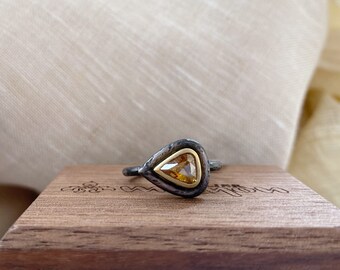May include: A pear-shaped ring with a yellow gemstone set in a gold bezel. The ring is made of oxidized silver and has a hammered texture.