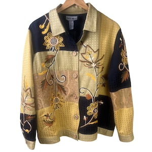 May include: A multi-colored jacket with floral embroidery. The jacket features a patchwork design with black, gold, and brown panels. The floral embroidery includes sunflowers and other stylized flowers. The jacket has a collared neckline and button closures.