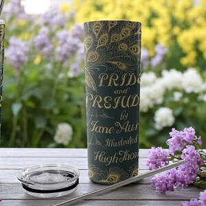 May include: Two stainless steel travel mugs with a peacock design and the text "Pride and Prejudice by Jane Austen Illustrated Hugh Thomson" on the side. The mugs are on a white surface with a straw next to each mug.