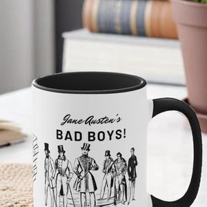 Pu&ograve; includere: Una tazza in ceramica bianca con bordo e manico neri. La tazza presenta un'illustrazione in bianco e nero di sei uomini in abiti del XIX secolo con il testo "Jane Austen's BAD BOYS!" e i nomi "Tilney, Willoughby, Crawford, Churchill, Elliot, Wickham" sotto.