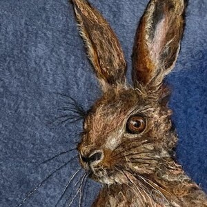 May include: A close-up of a brown rabbit with long ears and whiskers. The rabbit is looking to the right of the image. The background is a dark blue.