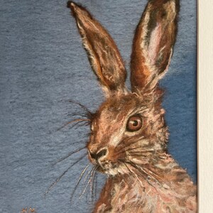 May include: A close-up of a needle felted artwork depicting a brown hare with a blue background. The hare is looking to the right of the image. The artwork is signed "H. Morley" and numbered "13/50".