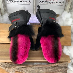 May include: A pair of pink and black fur mittens with a black buckle and the text "ART'ABASKA" in red on the top of each mitten.
