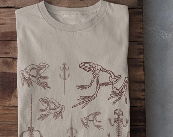 May include: A beige t-shirt with a print of multiple frog and lizard skeletons in a brown color.