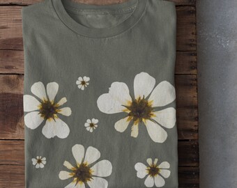 May include: A folded green t-shirt with a white floral print. The shirt has a crew neck and short sleeves. The flowers have brown centers.