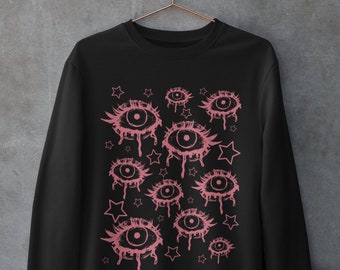 May include: Black sweatshirt featuring a pink eye and star pattern. The eyes are dripping with pink liquid.